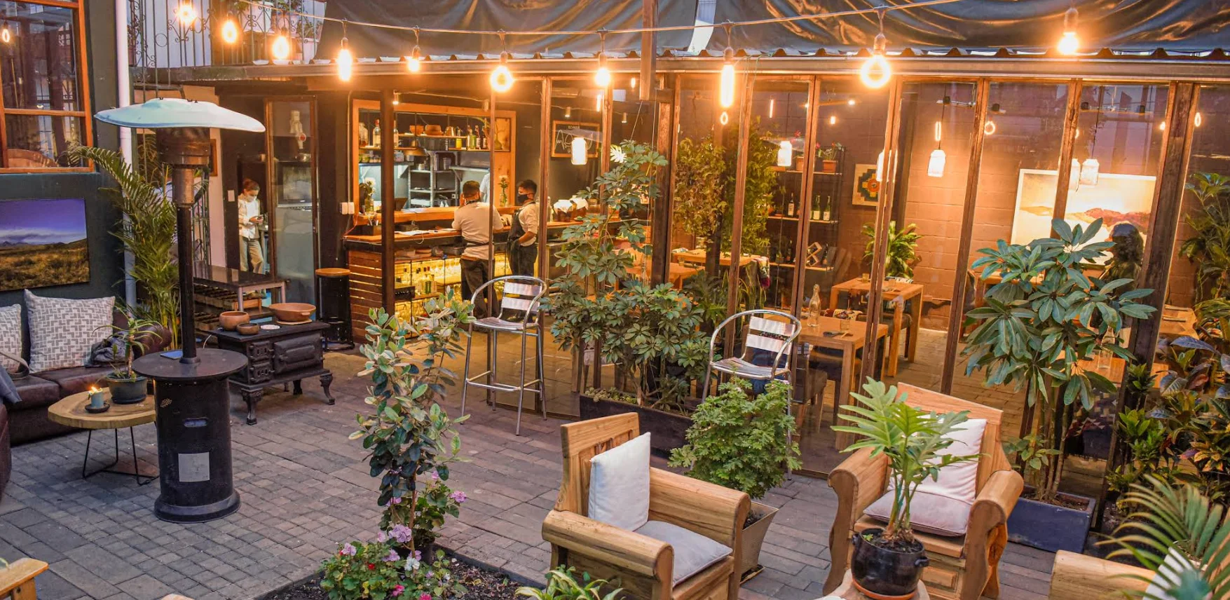 Terraza exterior de Restaurante Urko en Quito con iluminación de guirnaldas, muebles de madera y ambiente de jardín.